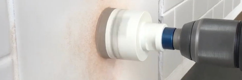 Diamond hole saw drilling a large hole through a white wall beside subway tile