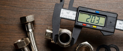 Digital caliper measuring a threaded pipe fitting on a wood bench