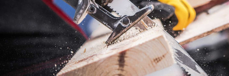 Reciprocating saw cutting through a wood beam, sawdust flying