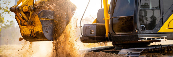 Excavator dumping a bucket of soil on a construction site at sunset