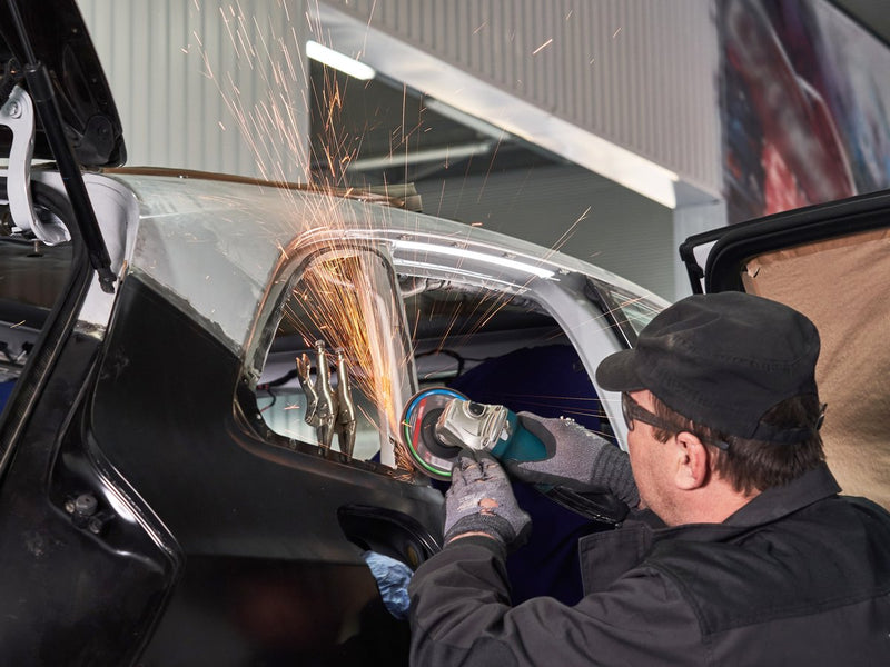 Technician grinding a weld seam on a car body panel, sparks flying