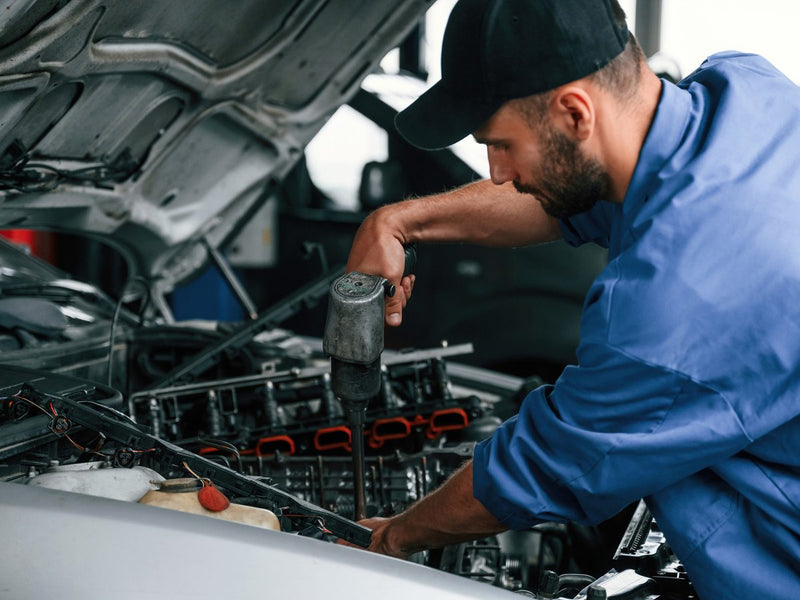 Mechanic using an impact driver on an engine under a raised hood