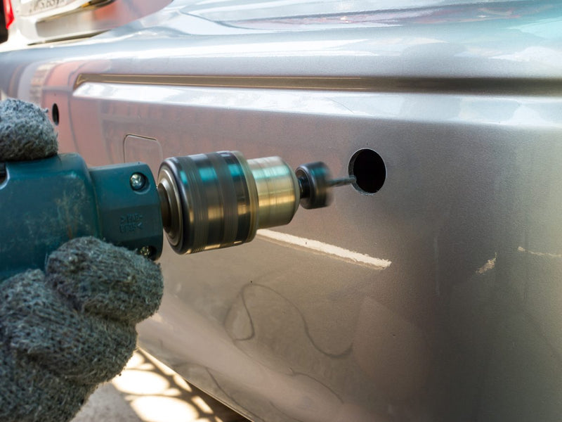 Technician cutting a parking-sensor hole in a bumper with a hole saw