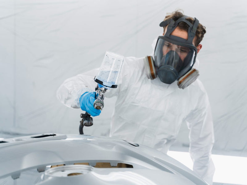 Painter in a respirator spraying a panel in a paint booth